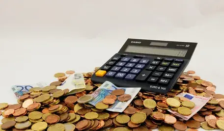 Kalkulator leżący na stosie monet i banknotów euro