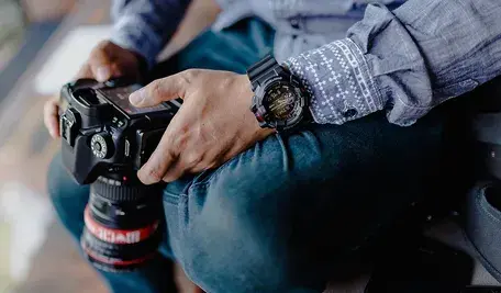 Mężczyzna trzyma aparat fotograficzny z dużym obiektywem, przygotowując się do robienia zdjęć; zbliżenie na dłonie i sprzęt fotograficzny.