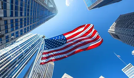 "Amerykańska flaga powiewa na tle drapaczy chmur Nowego Jorku – symbol zakazu wjazdu dla europejskich aktywistów DSA przez USA."