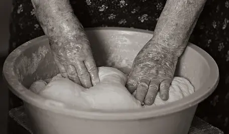 Ręce starszej kobiety ugniatającej ciasto w misce.