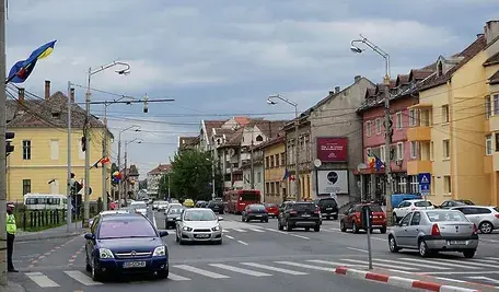 Ulica w rumuńskim mieście z ruchem samochodowym, kolorowymi kamienicami i rumuńskimi flagami zawieszonymi przy drodze