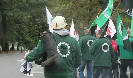 Górnicy w kaskach maszerują w grupie, niosąc flagi podczas protestu.