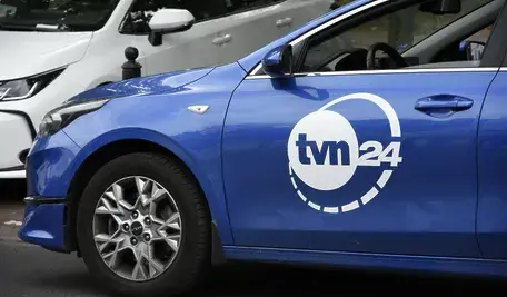 Samochód ekipowy TVN stojący przed siedzibą stacji — symbol działalności medialnej Warner Bros. Discovery w kontekście trwających rozmów o przejęciu firmy.