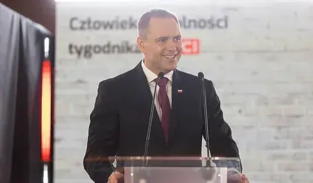 Prezydent Karol Nawrocki przy mównicy podczas wystąpienia publicznego na tle białej ściany.