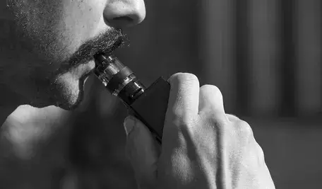 Mężczyzna używający elektronicznego papierosa, wydychający parę.