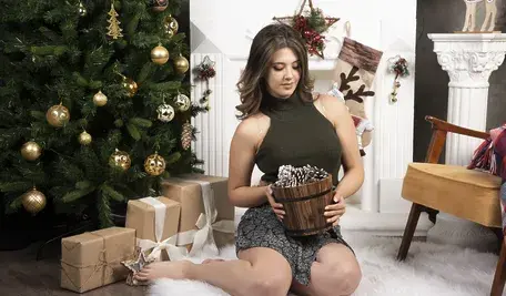 Młoda piękna kobieta pozuje z koszem szyszek w pobliżu choinki.