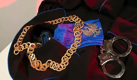 Sędziowski łańcuch z godłem Polski leżący na todze obok metalowych kajdanek.