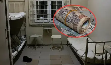 Cela więzienna z piętrowymi łóżkami, na pierwszym planie zwinięty plik banknotów zaznaczony czerwonym okręgiem