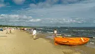 Letnia plaża w Świnoujściu nad Bałtykiem, z widokiem na spacerujących turystów i łódź ratunkową; w tle spokojne morze, gdzie kilka dni wcześniej doszło do makabrycznego odkrycia ludzkich szczątków dryfujących przy brzegu. 