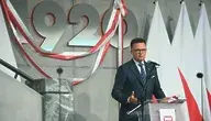 Szymon Hołownia przemawia podczas uroczystości w Muzeum Bitwy Warszawskiej 1920 roku, na tle polskich flag i symbolu 1920 – w kontekście doniesień o możliwej zmianie układu rządzącego i odsunięciu Donalda Tuska od władzy.