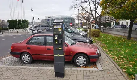 Samochód zaparkowany przy parkomacie w centrum miasta, kierowca dokonuje opłaty za parkowanie w strefie płatnego parkowania