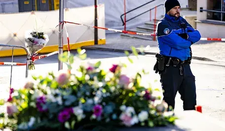 Wieniec złożony w miejscu tragedii, w tle stoi umundurowany policjant.