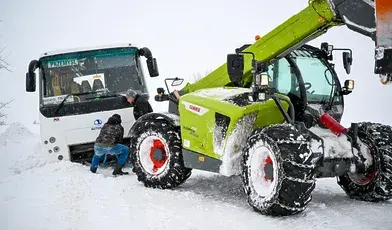Kierowca ciągnika uwalnia z zaspy autobus na drodze w Kupiatyczach w powiecie przemyskim