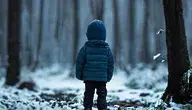 Dziecko w zimowej kurtce stojące samotnie w zaśnieżonym lesie.