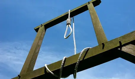 Drewniana szubienica z wiszącą pętlą na tle błękitnego nieba.