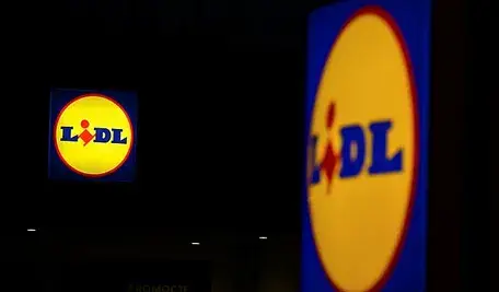 Logo sieci Lidl na elewacji sklepu nocą, podświetlony szyld widoczny na ciemnym tle.