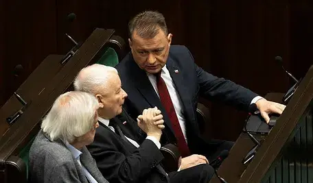 Jarosław Kaczyński siedzący na sali sejmowej w otoczeniu innych posłów PiS.
