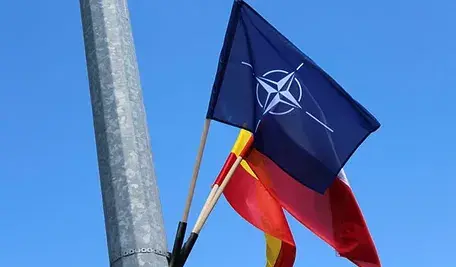 Flaga NATO powieszona na słupie wraz z innymi flagami.