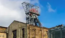 Wieża wyciągowa kopalni węgla z widocznym szybikiem i zabudowaniami przemysłowymi na tle błękitnego nieba.