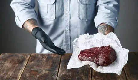 Mężczyzna w masarni trzyma świeżą, krwistą płat wołowiny, symbolizując brazylijski eksport mięsa – ale czy ukrywa toksyny z afery Carne Fraca? Zdjęcie ilustruje ryzyko dla Polski po umowie Mercosur.