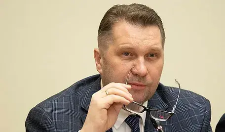 Przemysław Czarnek siedzący przy stole, trzymający okulary w dłoni, podczas oficjalnego posiedzenia.