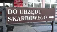Brązowy znak z napisem „Do Urzędu Skarbowego” i strzałką w prawo, umieszczony przed budynkiem instytucji publicznej.