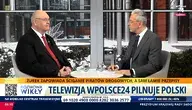 Telewizyjna rozmowa na żywo – dwóch mężczyzn w garniturach, aMarcin Wikło i prezes TK Bogdan Święczkowski siedzi przy stole w studiu, w tle zimowa sceneria miejska, na ekranie pasek informacyjny z hasłem o ściganiu piratów drogowych