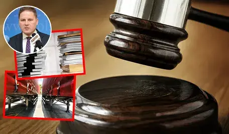 Młotek sędziowski na drewnianej podstawce na sali sądowej, a nałożone na niego czerwone ramki ze zdjęciami: z lewej strony portret mężczyzny przy mikrofonie z zasłoniętą twarzą, w środku stosy akt i dokumentów, na dole zaparkowane naczepy ciężarówek ustawione równolegle.