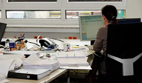 Kobieta pracująca przy biurku pełnym dokumentów.