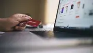 Dłoń trzymająca kartę bankomatową przed laptopem