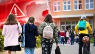 Dzieci idące do szkoły na tle symbolu alarmu ostrzegawczego – ilustracja kontrowersji wokół procedur bezpieczeństwa w placówkach oświatowych