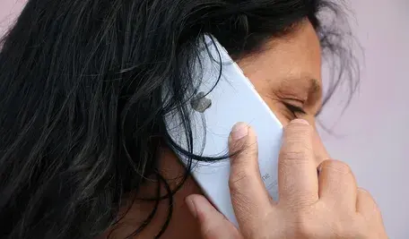 Kobieta w czarnych włosach trzymająca przy uchu biały telefon.