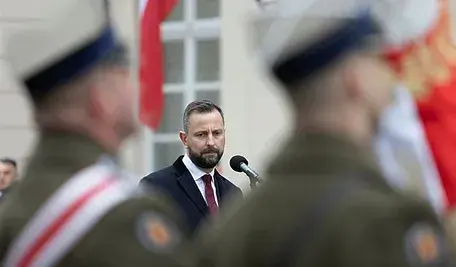 Władysław Kosiniak-Kamysz przemawiający przed mikrofonem widoczny między dwoma rozmazanymi żołnierzami Wojska Polskiego.