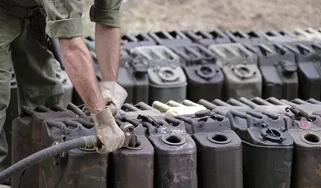 Pracownik w rękawicach napełnia kanistry paliwem – rzędy metalowych pojemników z paliwem ustawione na zewnątrz