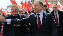 Prezydent Karol Nawrocki witający się z obywatelami na tle powiewających biało-czerwonych flag.
