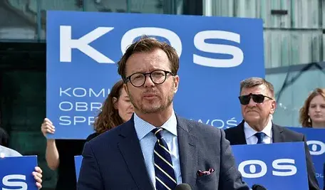 Europoseł Koalicji Obywatelskiej Michał Wawrykiewicz podczas konferencji prasowej na tle niebieskich transparentów..