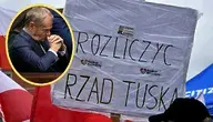 Biały transparent z hasłem: "rozliczyć Tuska" i zdjęcie premiera.