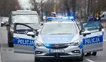 Radiowóz policyjny z włączoną sygnalizacją świetlną i stojący obok policjant.
