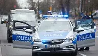 Radiowóz policyjny z włączoną sygnalizacją świetlną i stojący obok policjant.