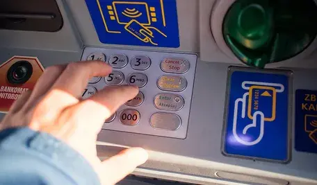 Dłoń osoby wypłacającej pieniądze z bankomatu.