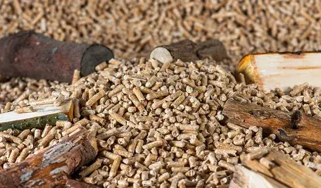 Pellet drzewny do ogrzewania – granulat z biomasy rozsypany na tle kawałków drewna opałowego