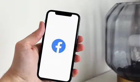 Dłoń trzymająca telefon z wyświetlonym logo Facebooka