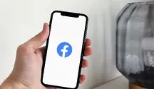 Dłoń trzymająca telefon z wyświetlonym logo Facebooka