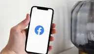 Dłoń trzymająca telefon z wyświetlonym logo Facebooka