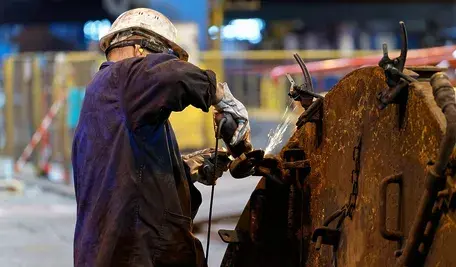 Pracownik przemysłowy szlifujący metal przy użyciu szlifierki kątowej w hali produkcyjnej