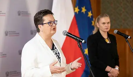 Wiceminister edukacji Katarzyna Lubnauer z szefową resortu na konferencji prasowej na tle flagi Polski i Unii Europejskiej.