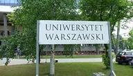Biała tablica z napisem Uniwersytet Warszawski stojąca na tle drzew.