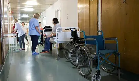 Pacjenci oraz pielęgniarki w korytarzu szpitalnym.