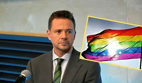 Rafał Trzaskowski podczas wystąpienia, obok zdjęcie tęczowej flagi.
