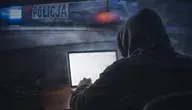 Mężczyzna w kapturze siedzący przed laptopem, w tle sygnalizacja świetlna radiowozu policyjnego
